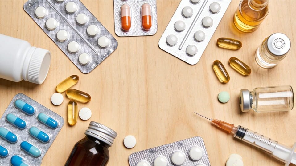 Tablets, capsules, blister packs, vials and a syringe on a wooden table